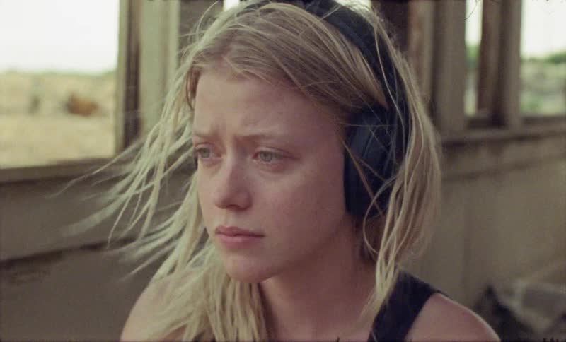 A young woman listening to headphones in a dilapidated building as winding whips through her hair