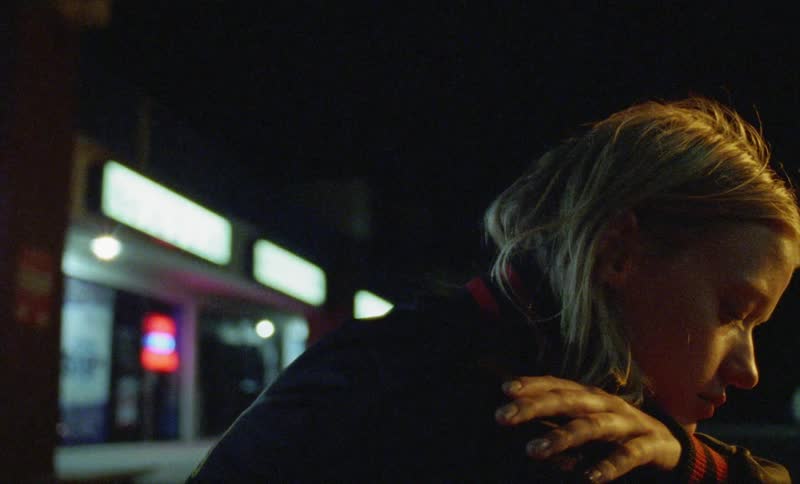 A woman is sitting outside by a store at night