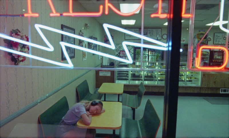 A young woman wearing headphones resting her head on a table in a small diner