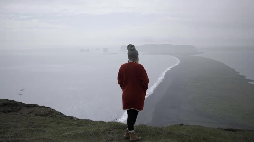 Woman stands near edge looking at shoreline below