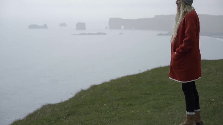 A woman stands on grass near cliff edge