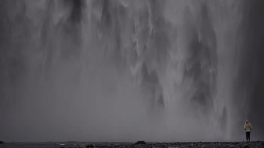 A person is standing before a large waterfall