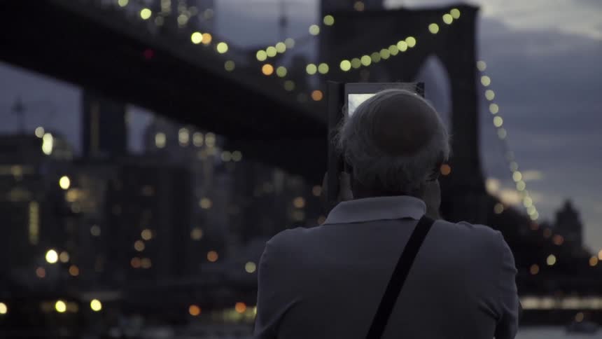 Person taking a picture of a bridge and a large city on their tablet at dusk