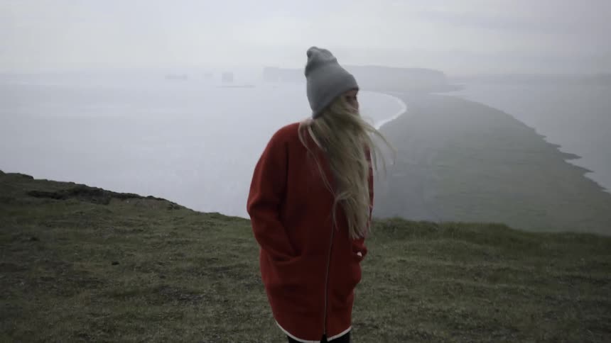 A woman is walking along a cliff by the water on a foggy day