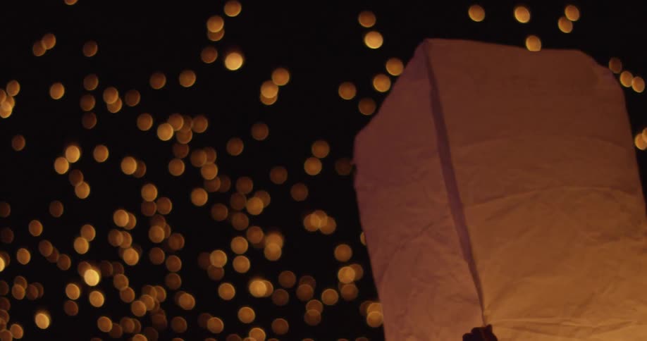 Someone holding on to a lighted chinese lantern while lights flicker in the sky above