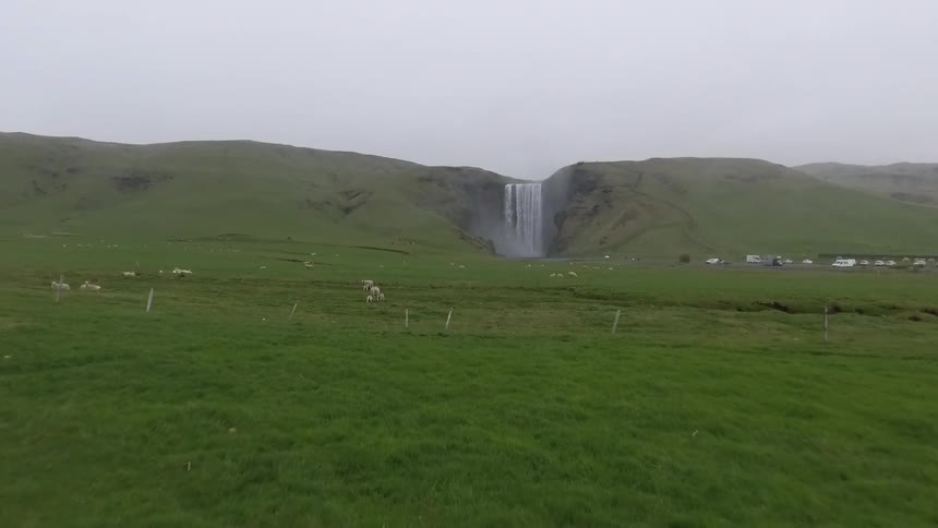 A large field with sheep leads to a waterfall