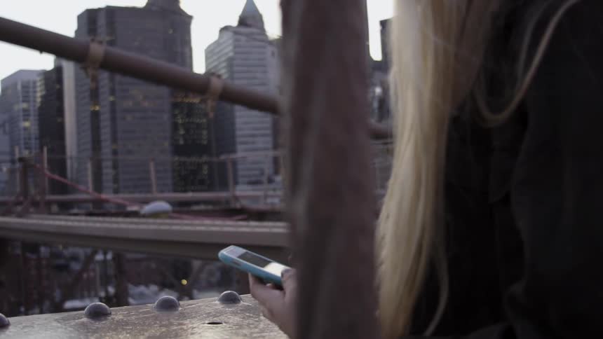 Woman touching her phone while looking at a city from a bridge