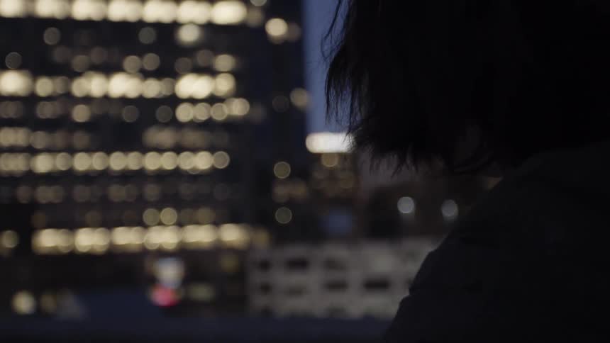 Woman stands on balcony looking at smartphone with city in the background