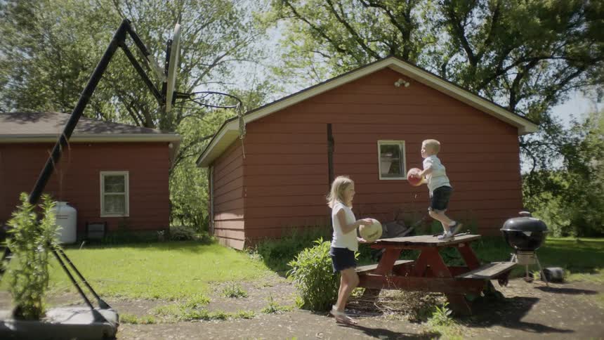A boy and a girl in a backyard playing with balls and a basketball hoop