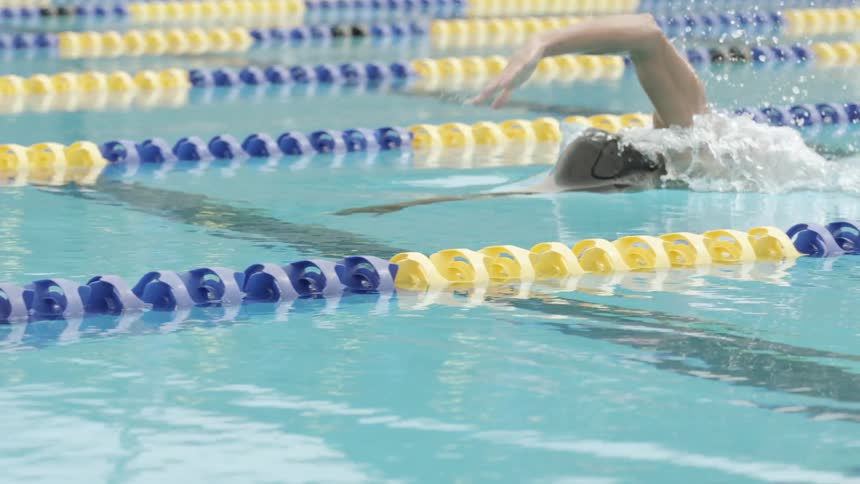 A male swimmer is swimming through a floating lane in an indoor pool