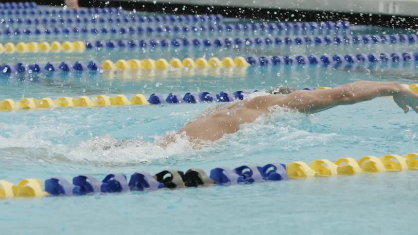 A man swims freestyle in a lane in a swimming pool