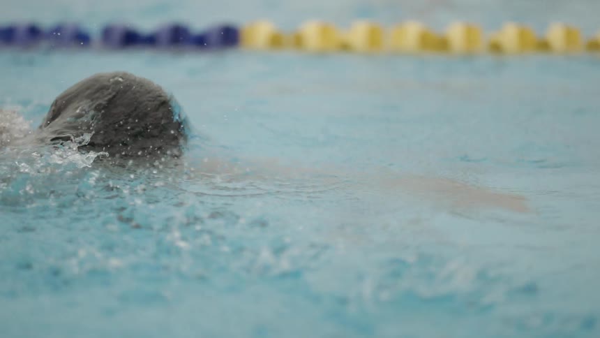 A male swimmer is racing down a lane in a swimming pool while swimming freestyle