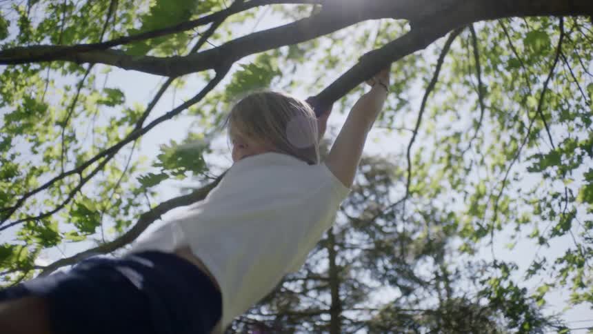 A young white girl swings back and forth from a tree branch and then lets go