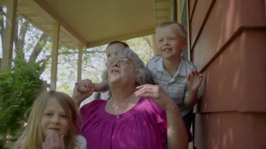 A grandmother and her grandkids on a porch talking and laughing