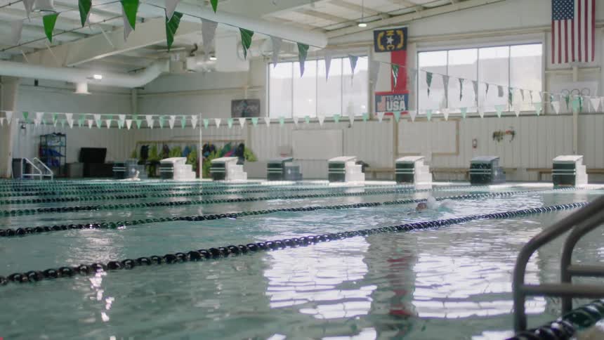 Two people swim down lanes in a mostly empty olympic sized swimming pool