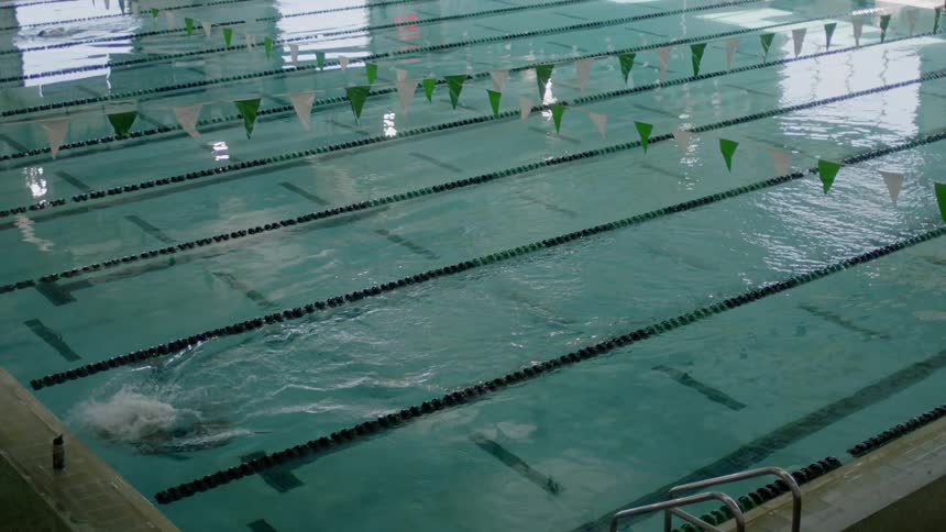 A female swimmer is swimming laps through two racing lanes of an indoor pool