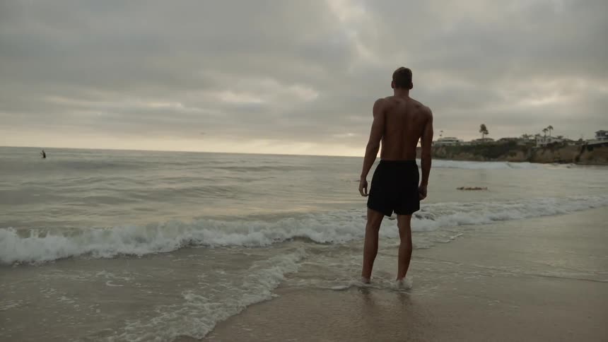 A shirtless man stands on the beach