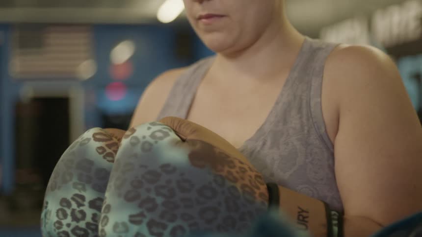 Woman wears boxing gloves and checks them in the gym