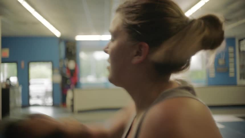 A white female is using boxing gloves to punch a punching bag in a gym lit with an abundance of natural light