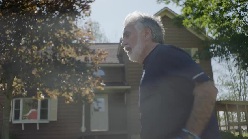 An elderly man jogging through a neighborhood during the day