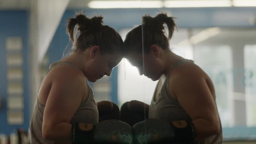 A woman with boxing gloves leaned up against a mirror
