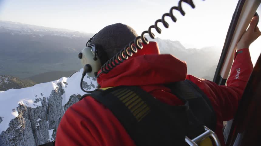A man sits on the edge of plane while looking down at the snow covered mountains