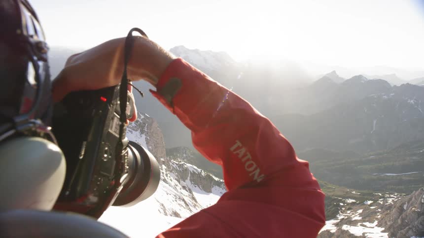 A man takes photos of a mountain range from the inside of a small aircraft
