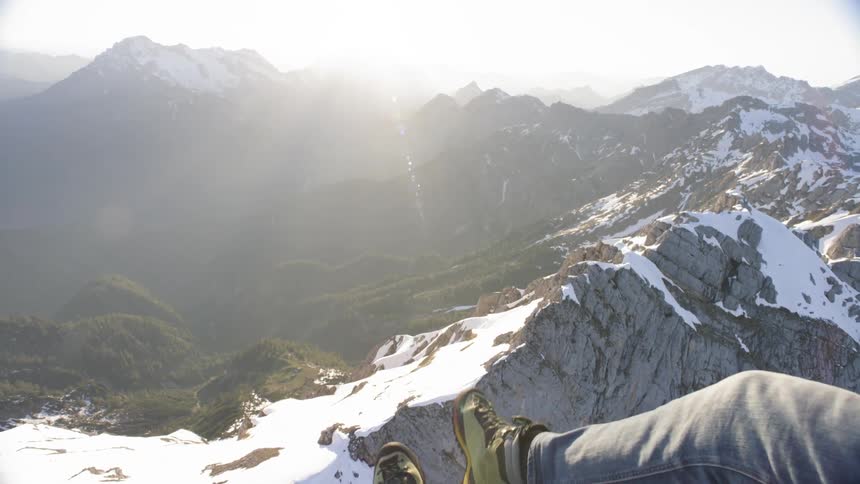 A man hangs his legs out of a small aircraft while flying over a mountain range