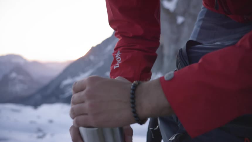 A man in a winter jacket opens a metal thermos