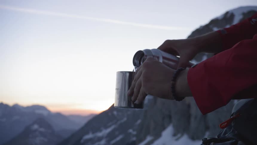 Hands holding a cup pouring water from metal thermos in the mountains