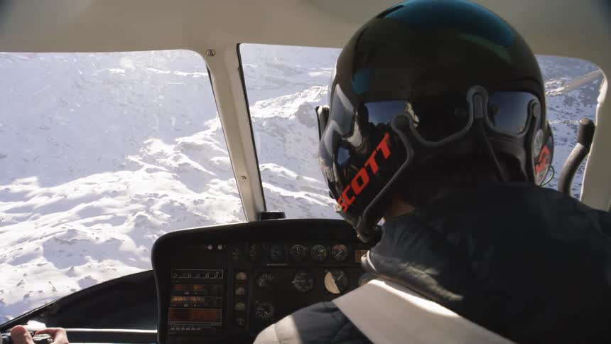 Pilot flying a helicopter over a mountain