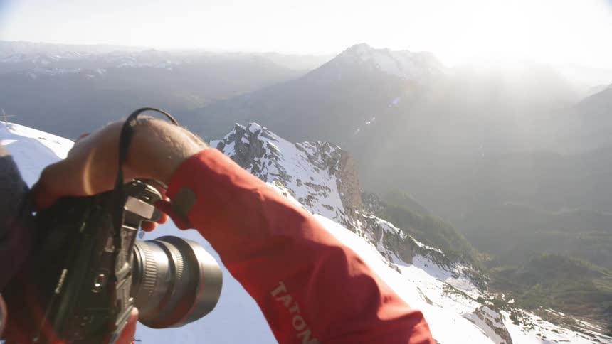 A man is taking photographs from the top of a snow covered mountain