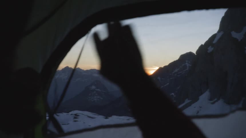 A person is zipping a tent outdoors by a mountainous area