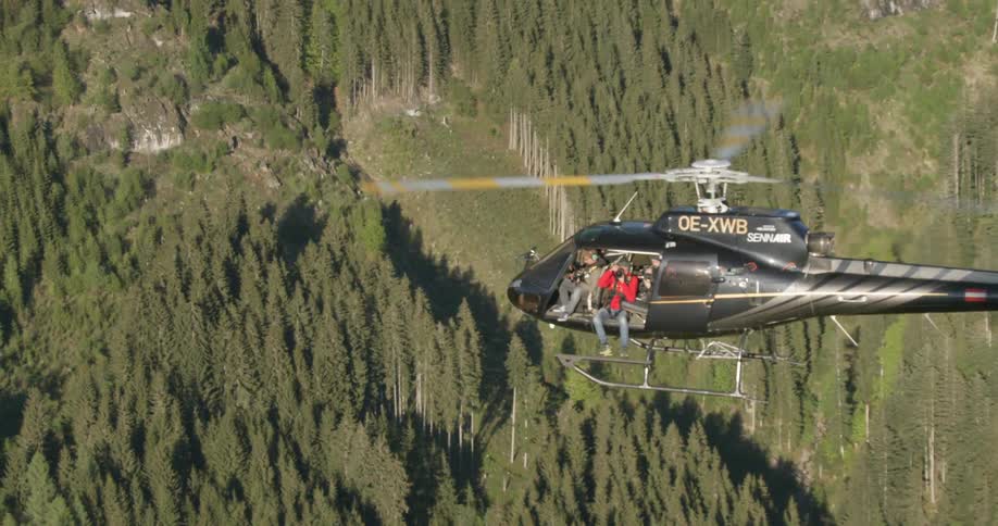 A helicopter flies over a forest with a camera man taking pictures