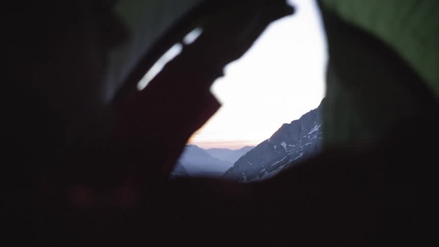 A man inside a tent zips the flap on a snowy mountain view