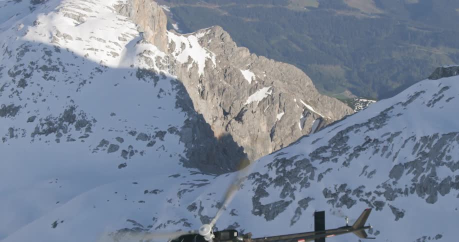 A helicopter soars high above a very tall mountain range that is coated in snow