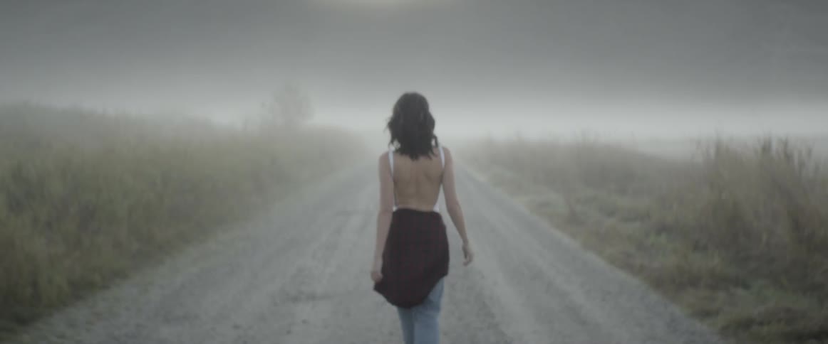 Woman walks down the road through the mist near the fields