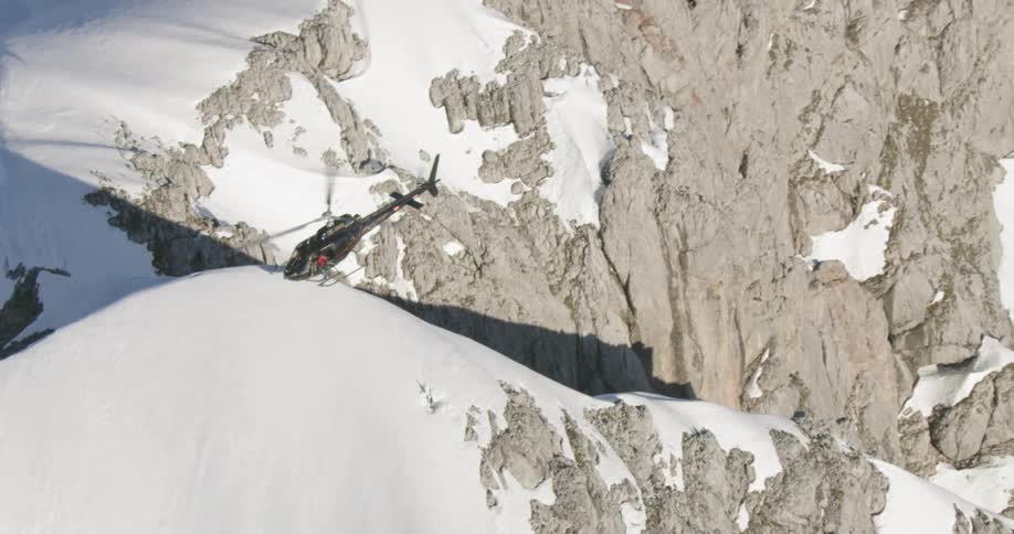 A helicopter is hovering over the snow on the mountain