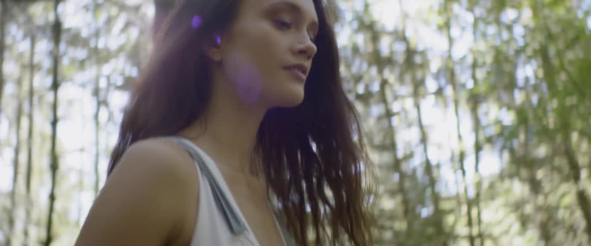 A woman in denim overalls walks alone in a sunny forest