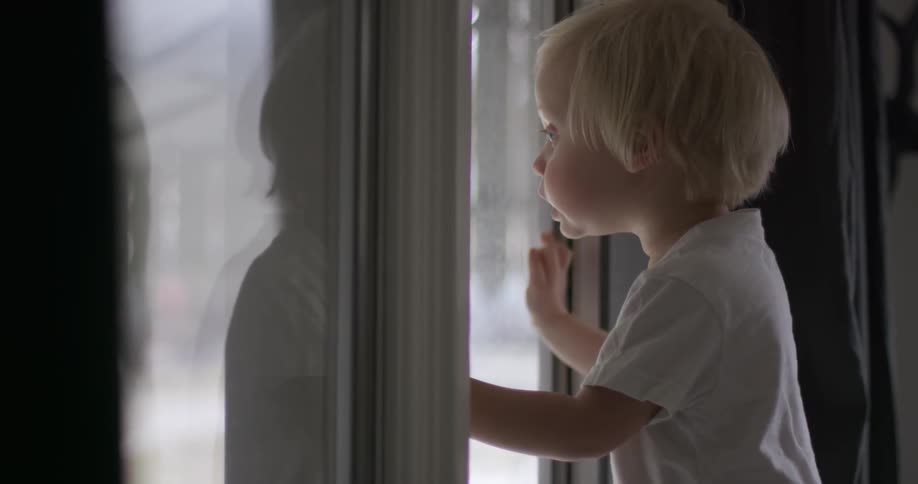 A boy is leaning against some glass looking outside