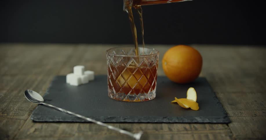 Beverage is being poured into a glass as an orange sits nearby