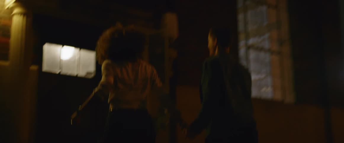 A man and a woman holding hands while going into a building at nighttime