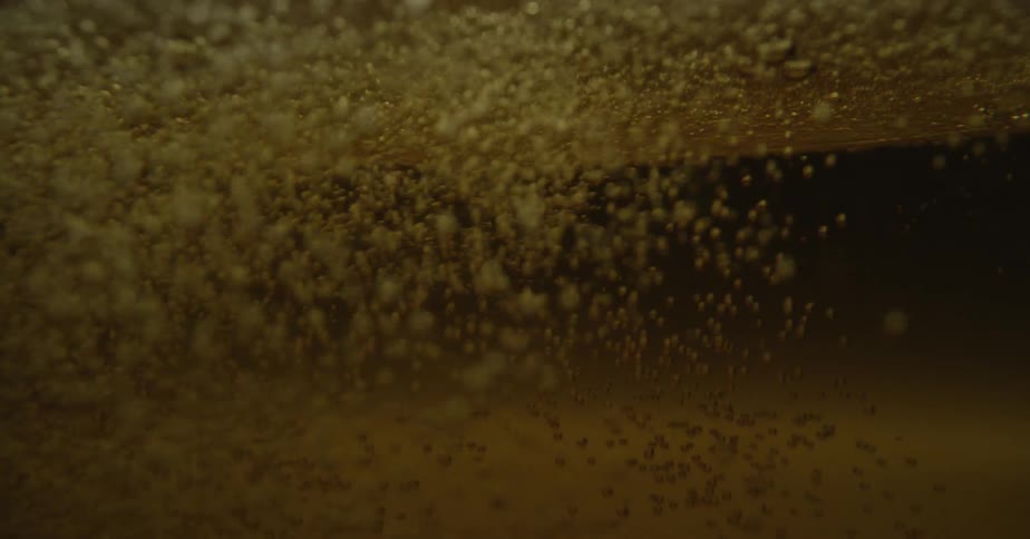 From below the surface of the amber tinted liquid countless bubbles are seen rising up to the surface of as more liquid is poured in