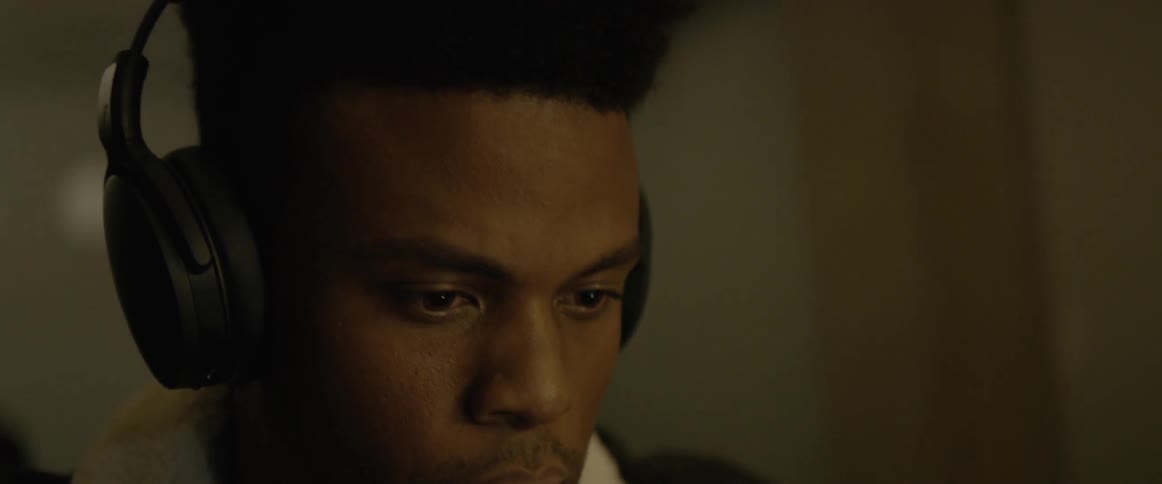 A man wearing headphones nods while looking at a monitor