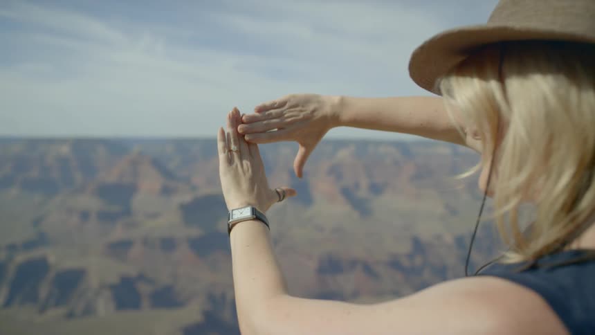 A blonde woman frames a canyon view with her hands