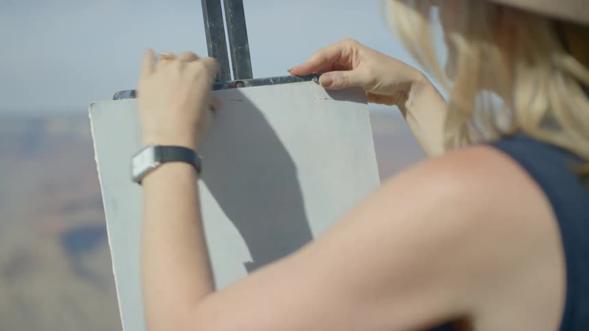 A blonde woman sets up a tripod for an art canvas
