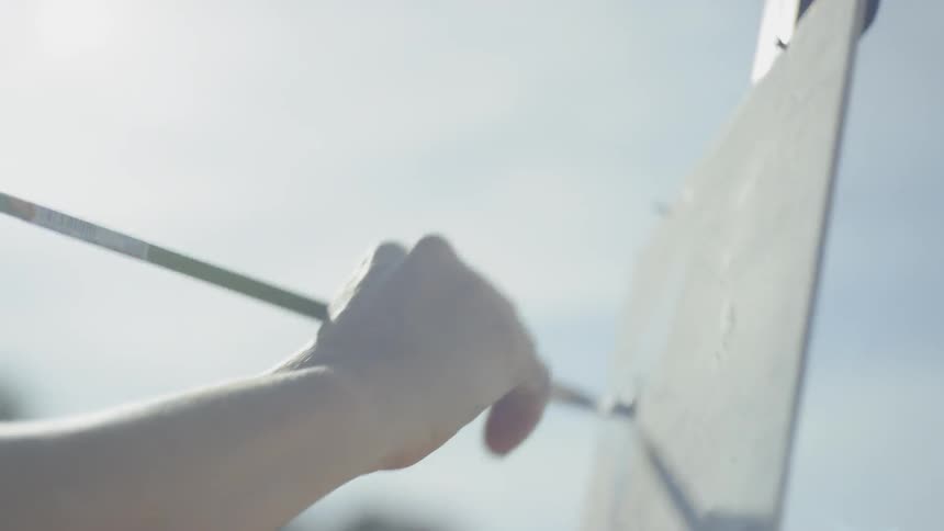 A woman wearing a hat is painting onto a canvas held up by an easel atop a mountain