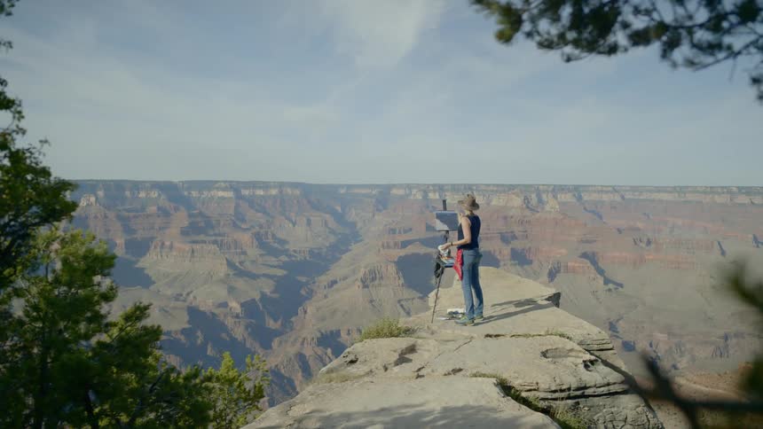 A woman stands on top of a mountain and paints