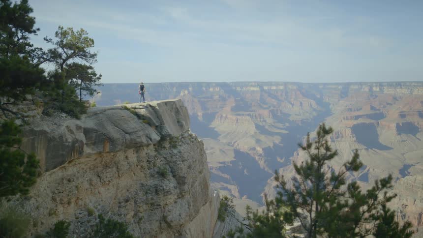 A woman wearing a hat is painting onto a canvas held up by an easel atop a mountain