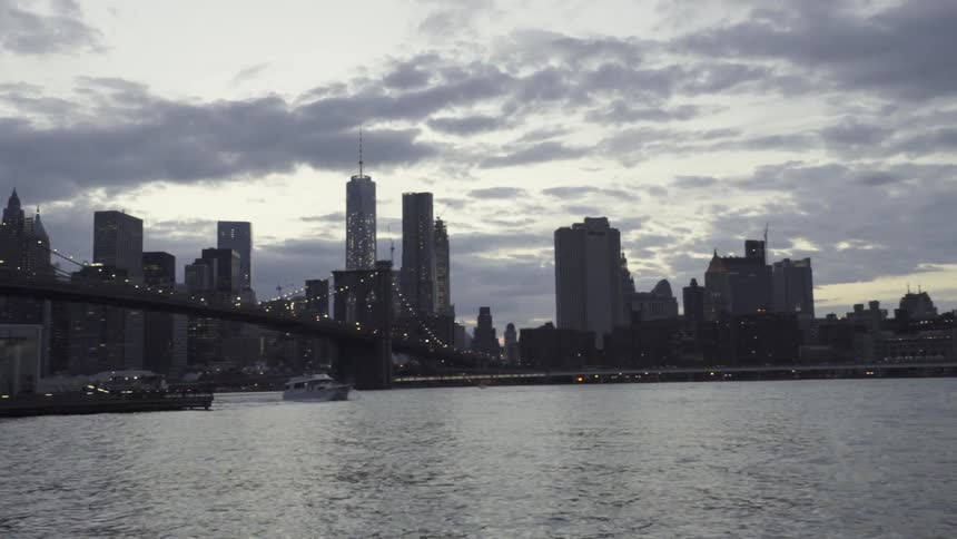 Boat crosses under Brooklyn bridge at dusk
